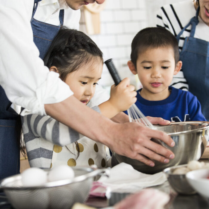 Little girl and her brother with her two parents, whisking ingredients in a metal bowl