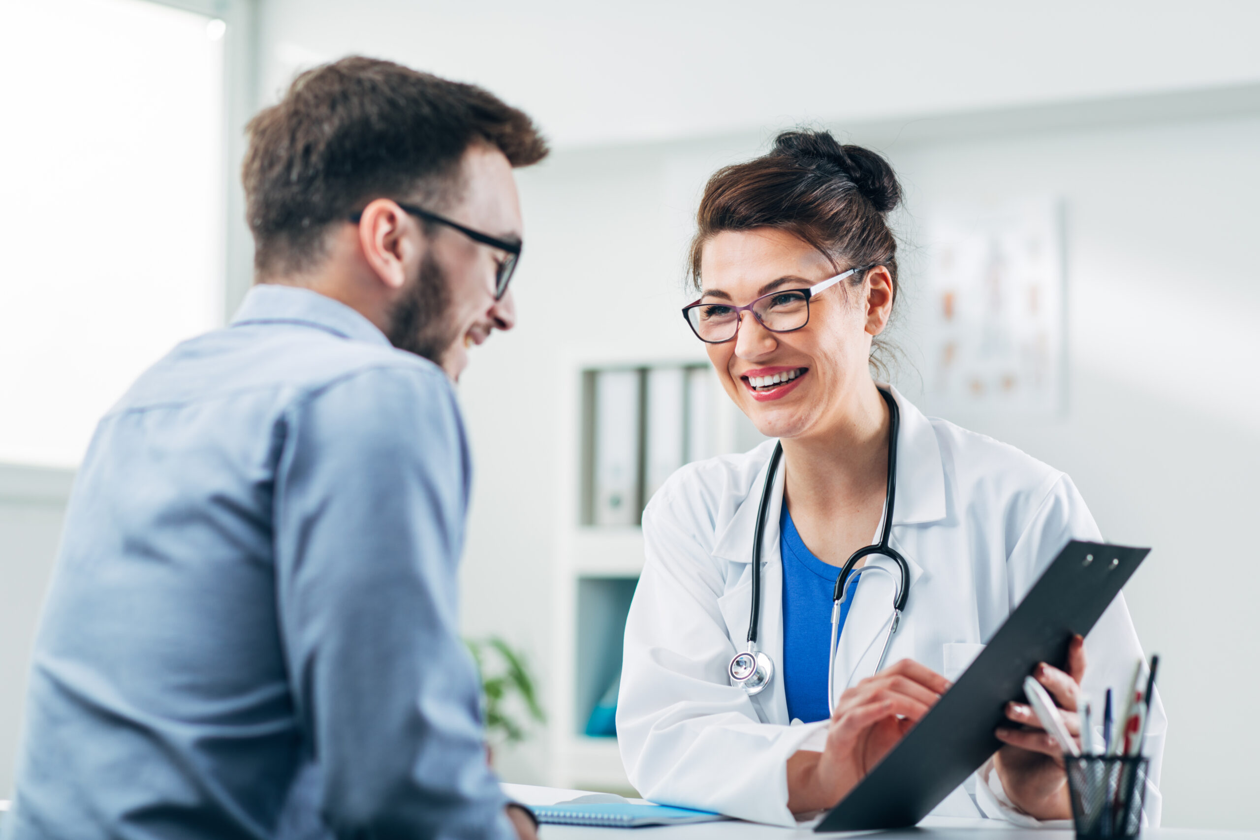 Female doctor sitting at desk pointing to patient's information while patient looks at document and smiles