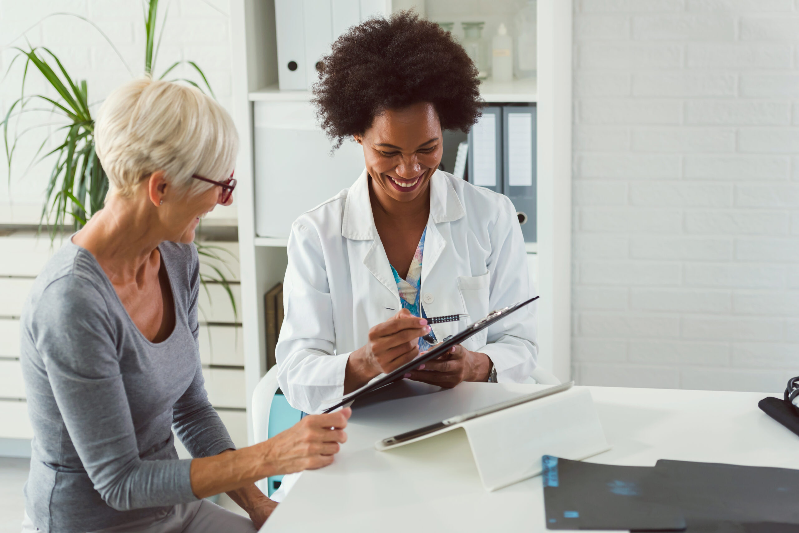 Female doctor in lab coat sitting at table while elderly patent reviews information with her.