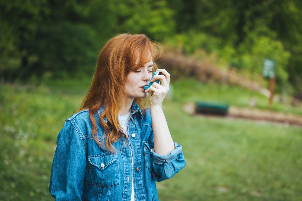 Young woman standing outside using inhaler to treat asthma