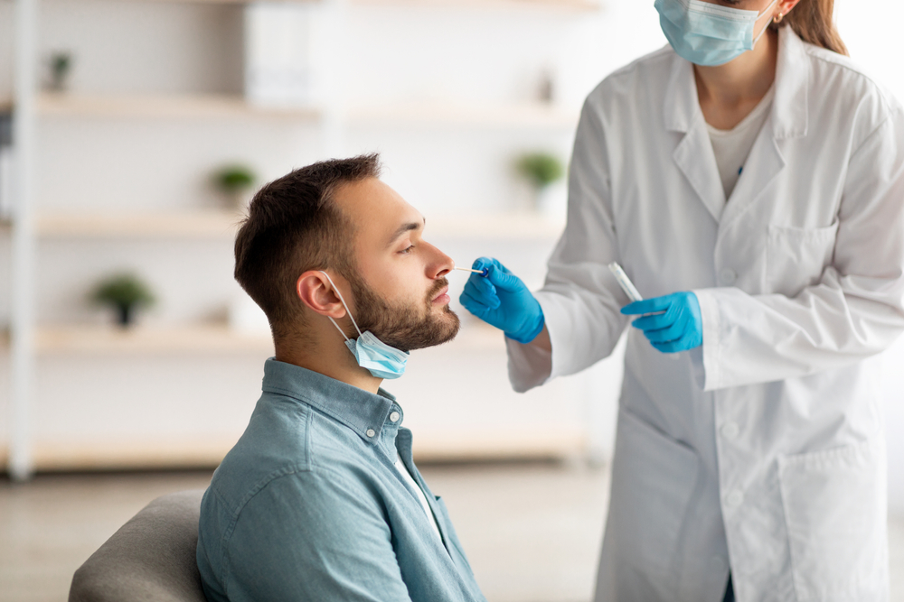 man receiving a medical test with cotton swab in his nose administered by female medical professional in a mask and gloves