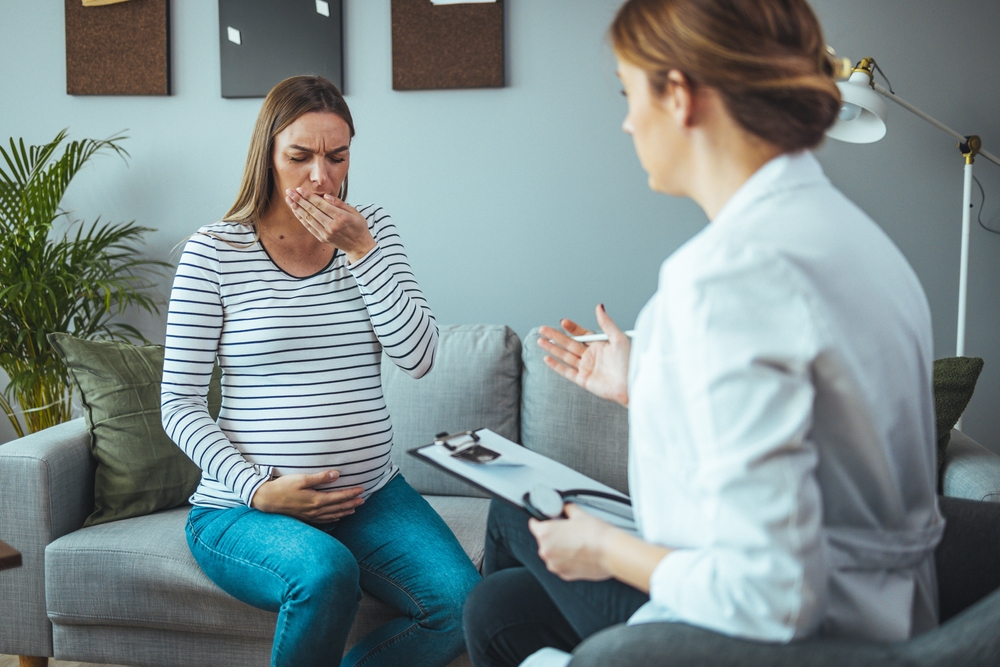 pregnant woman coughing while sitting with medical doctor in a consultation room