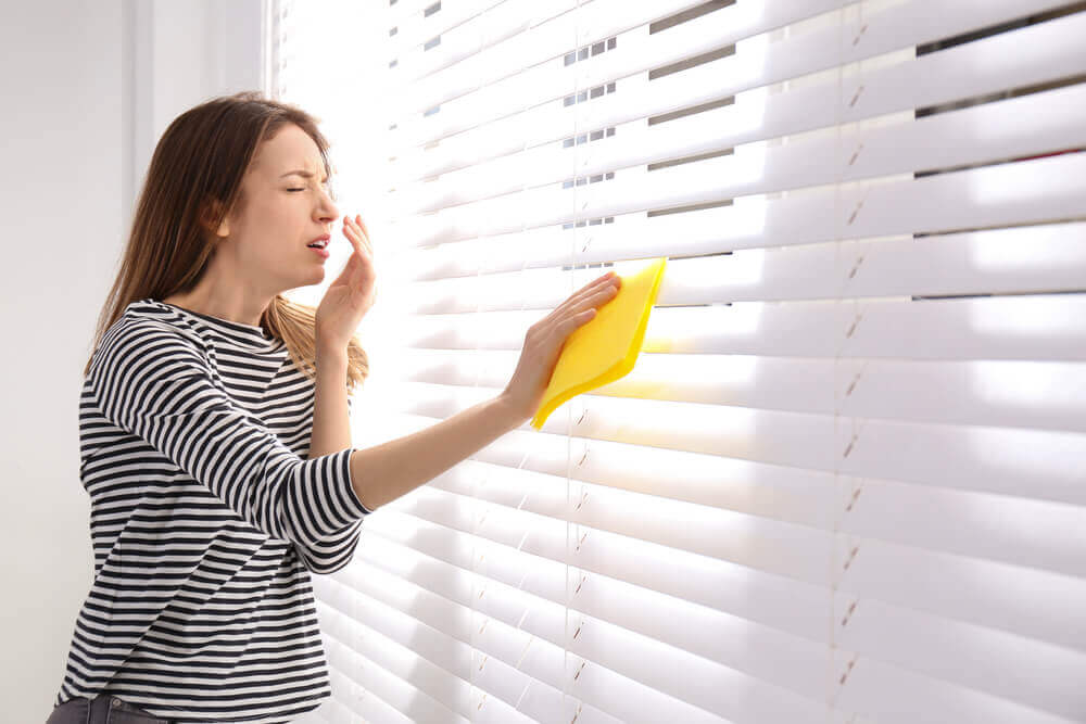 woman sneezing while dusting blinds