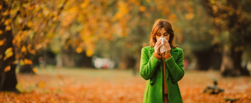 Woman sneezing with Fall trees in the background